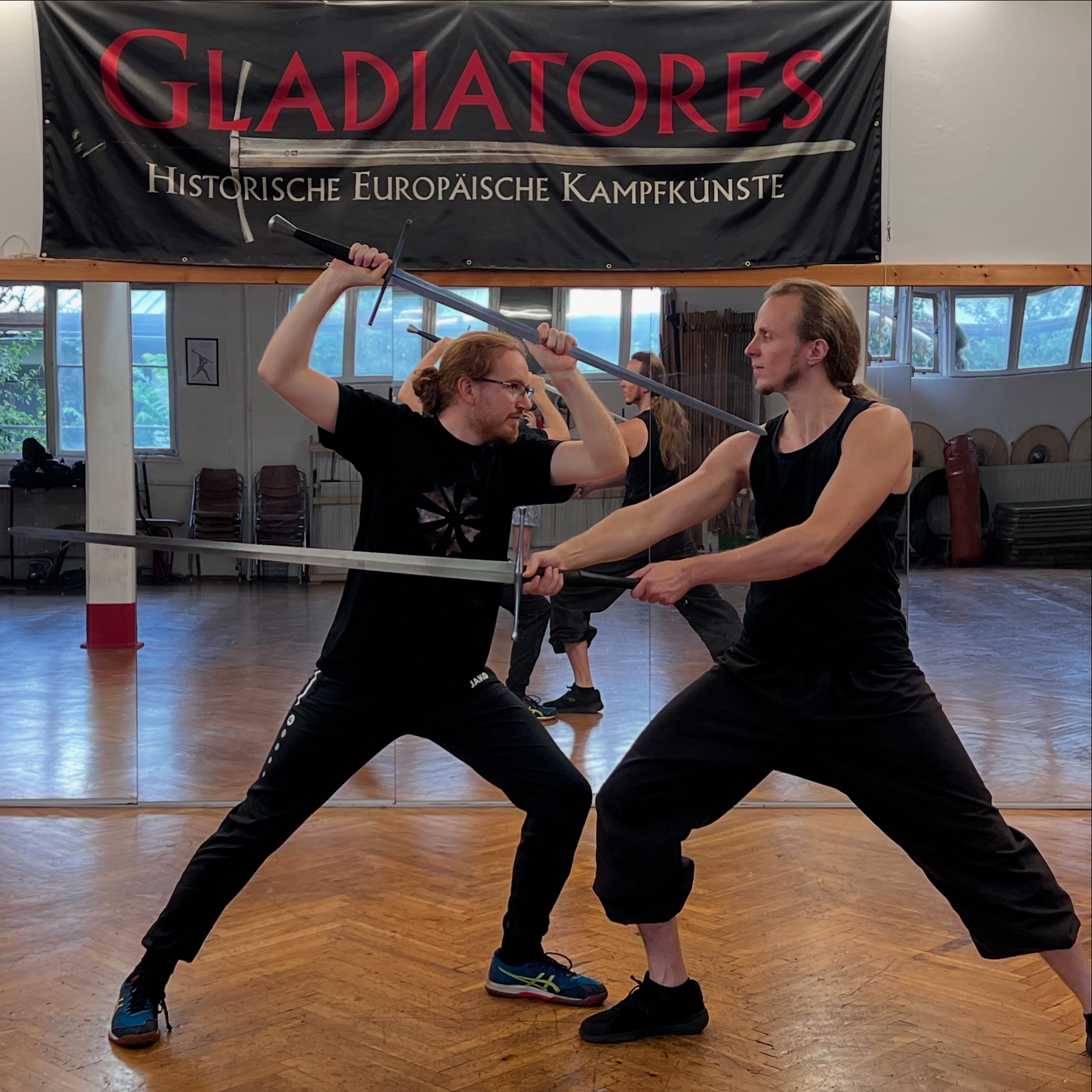 Two fencers with longswords under the Gladiatores banner in the Mühlburg hall