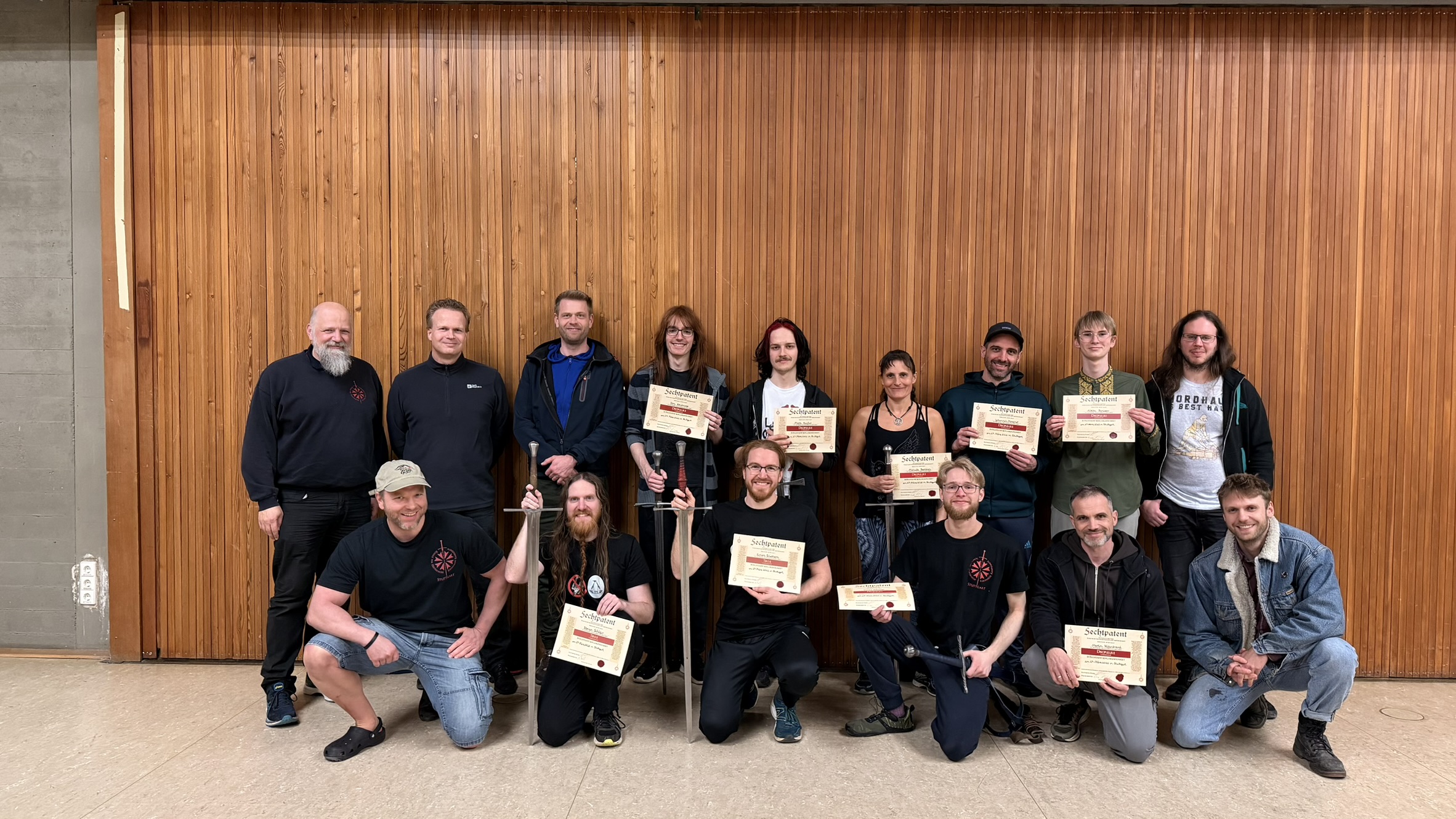 Group of fencers with their fencing certificates after the exam, holding longswords in the hall